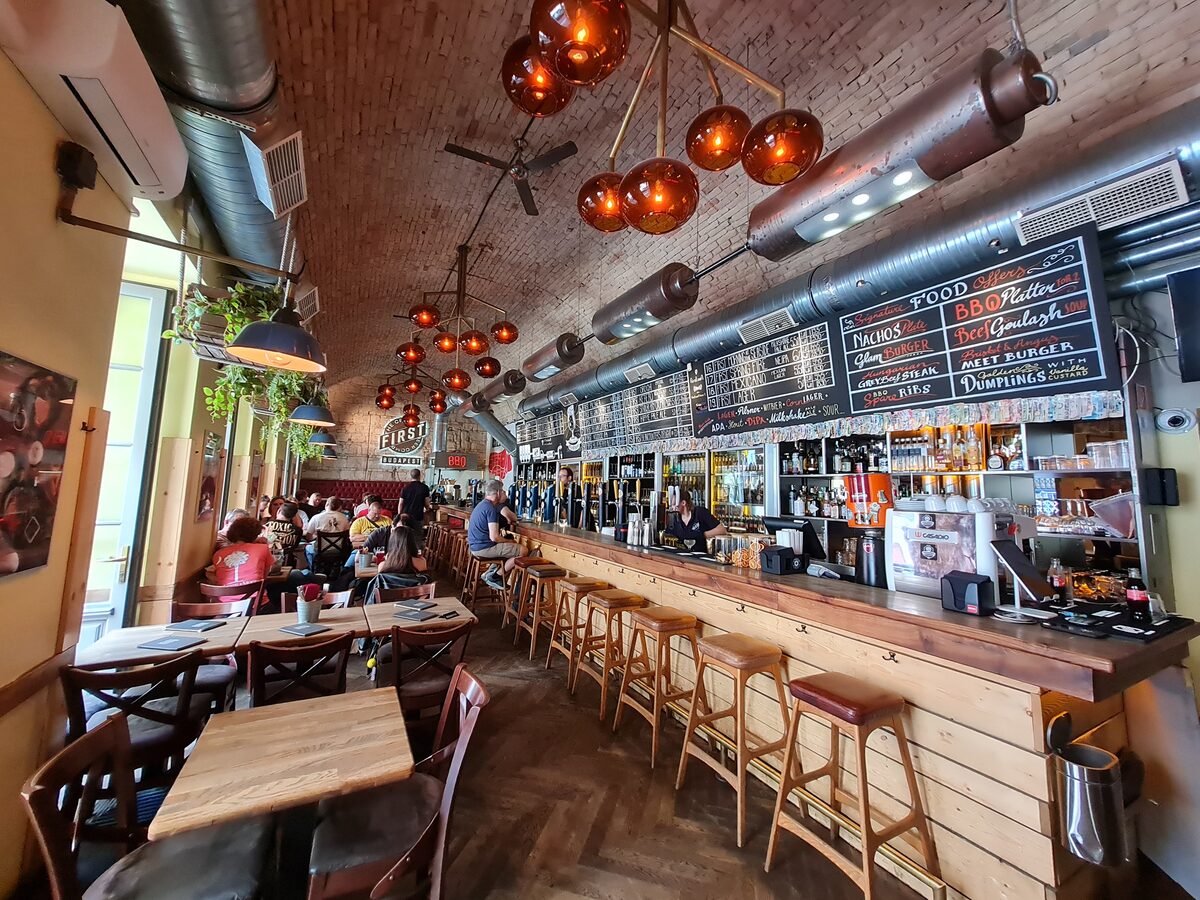 Industrial interior of First Craft Beer and BBQ Budapest with vaulted brick ceiling amber pendant lights and long wooden bar