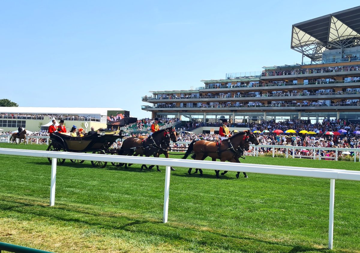 King Charles in the Royal Procession landau at Royal Ascot, escorted by scarlet-liveried outriders in front of packed grandstands