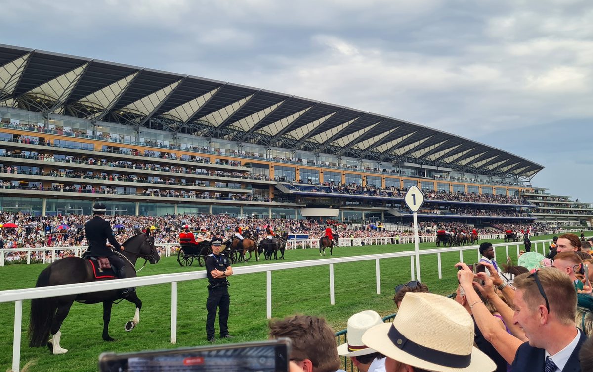 The Royal Procession at Royal Ascot — horse-drawn landau carriages escorted by mounted cavalry in front of packed grandstands