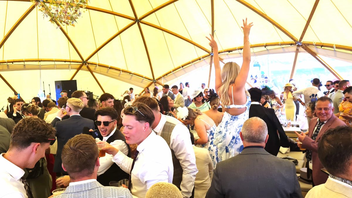 Packed Village Enclosure dome tent at Royal Ascot with racegoers dancing and raising their hands