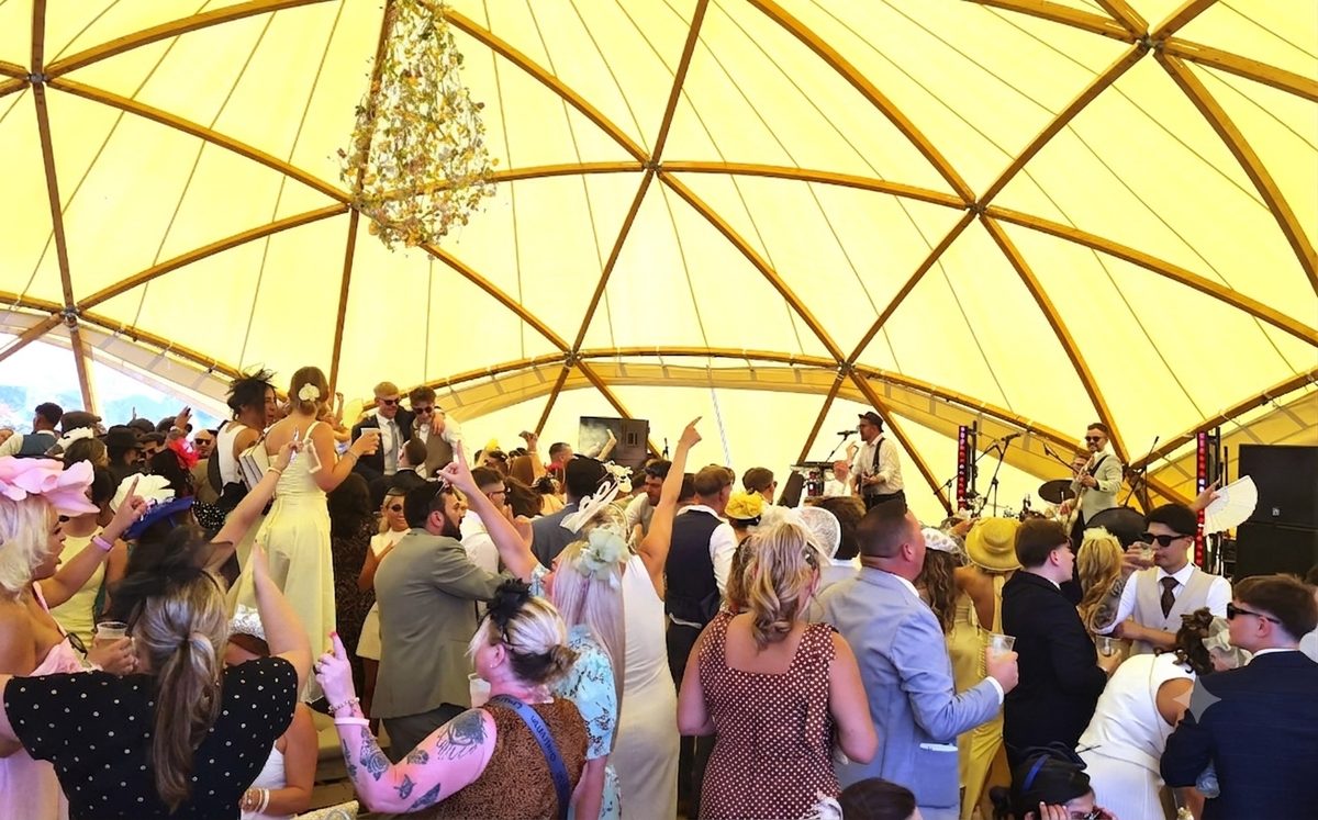 Packed Village Enclosure dome tent at Royal Ascot with crowds dancing to a live band under a yellow canopy