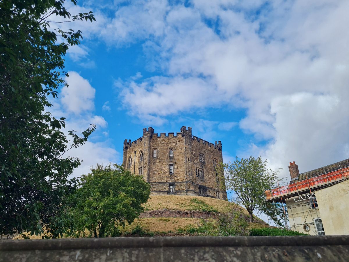 The keep of Durham Castle standing on its grassy motte against a blue sky