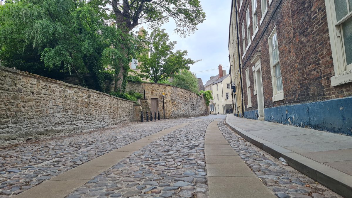 Cobbled street rising uphill towards Durham Cathedral, with a high stone wall alongside