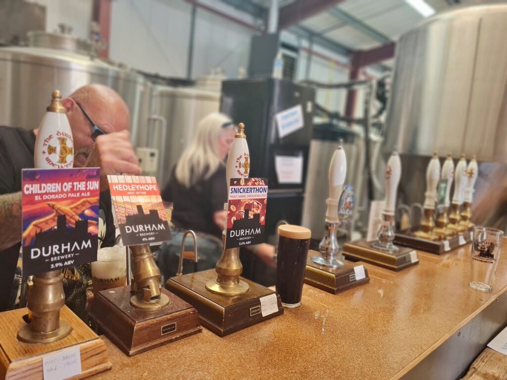 A row of handpulls with Durham Brewery pump clips in front of the fermenting vessels