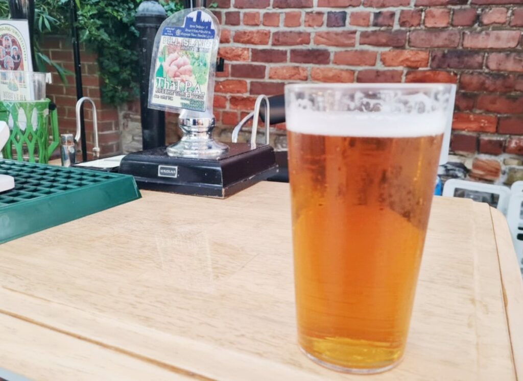 A pint of Hill Island pale ale on a wooden table with the pump clip behind