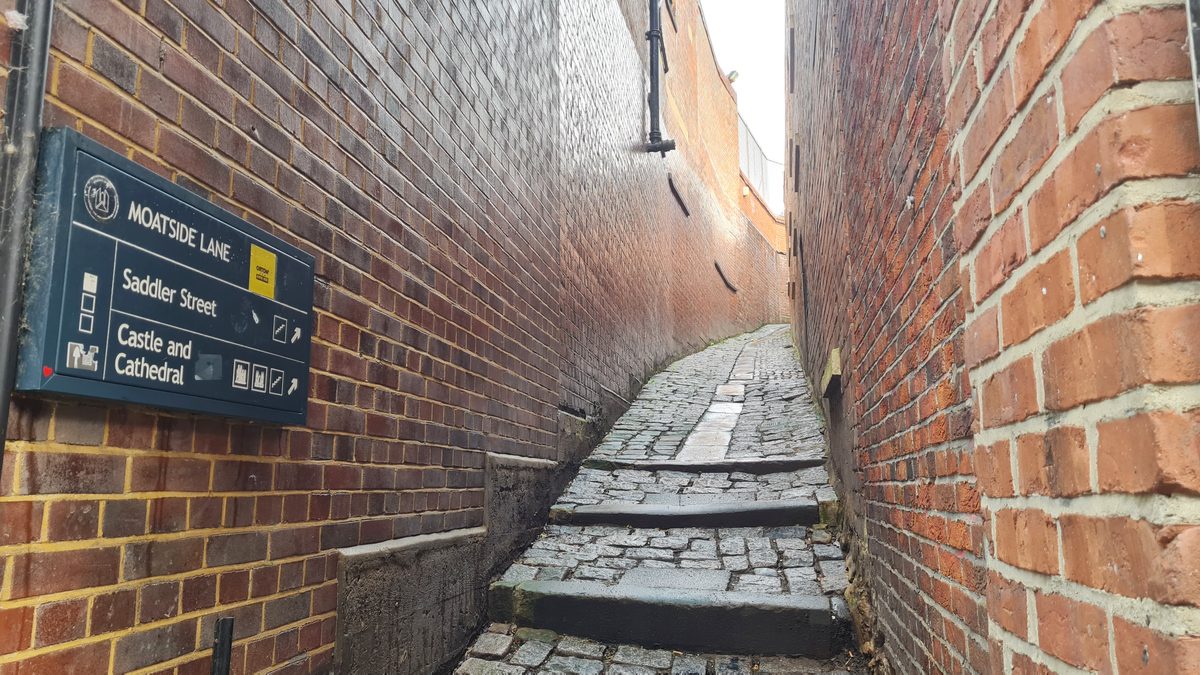 Narrow brick vennel with worn cobbled steps and a Moatside Lane signpost, Durham