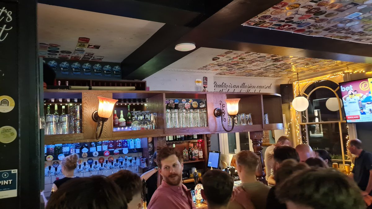 The Corner House Windsor — busy bar interior at night with tap handles and beer mat ceiling