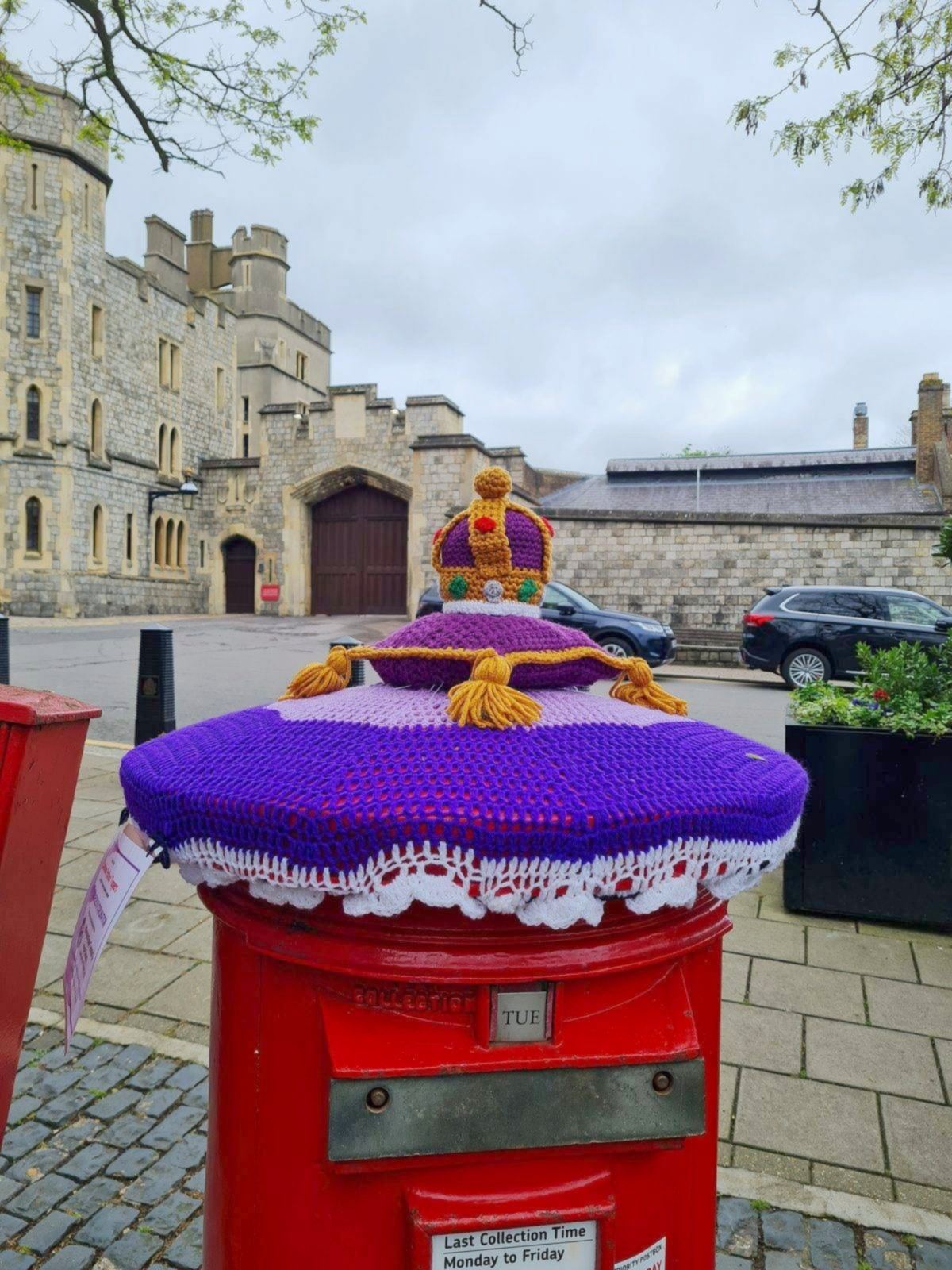 Purple crochet postbox topper with a gold crown and tassels on a red postbox in Windsor