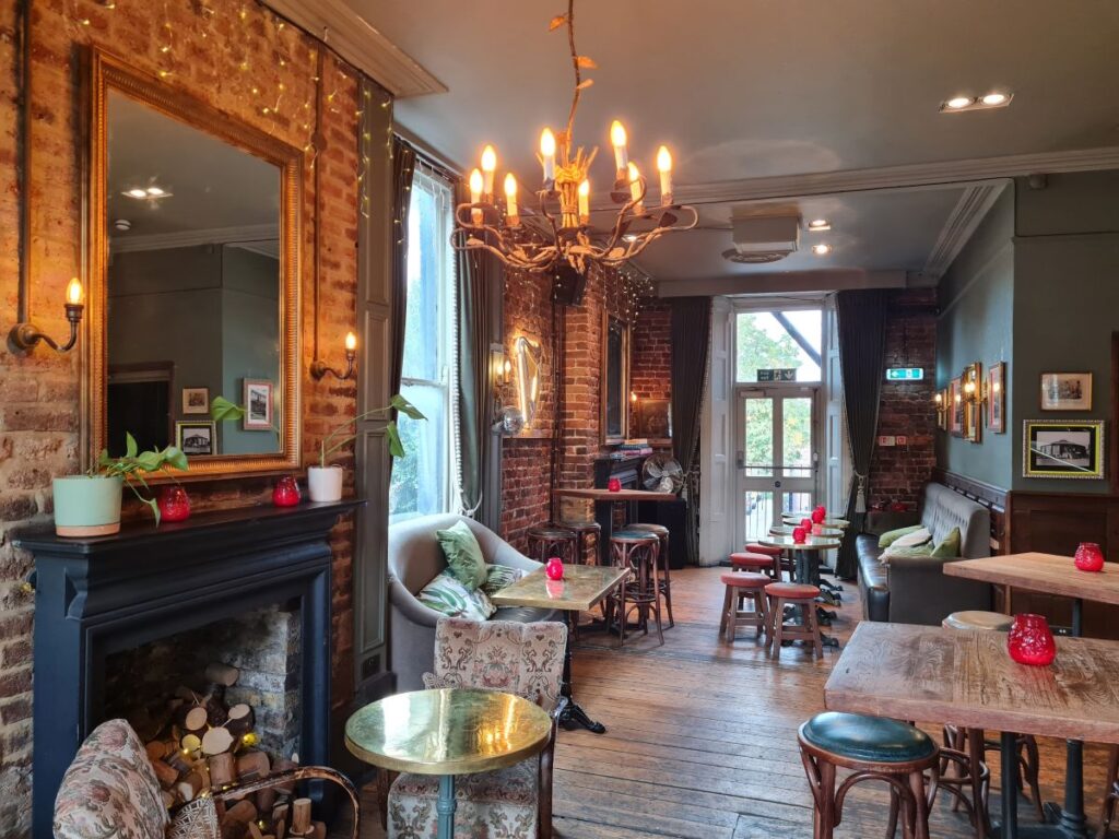 The upstairs room at the Lock Tavern in Camden — exposed brick, a fireplace, a chandelier and mismatched armchairs