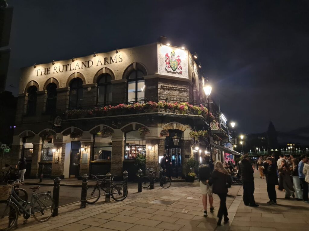 The Rutland Arms on the Hammersmith riverside at night, lit up with hanging baskets along the first floor