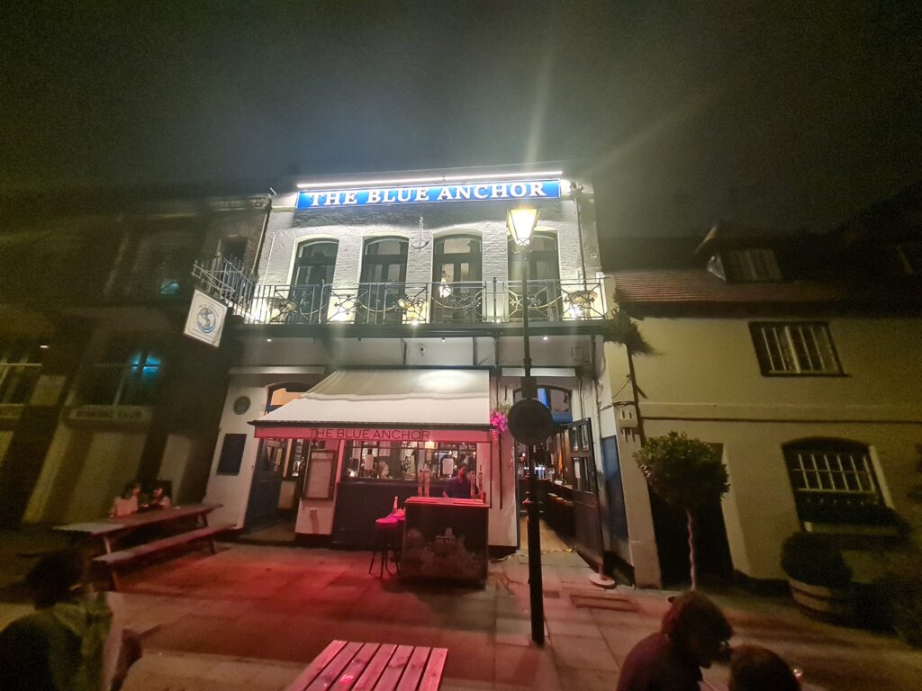 The Blue Anchor pub lit up at night on the Hammersmith riverside, with benches outside