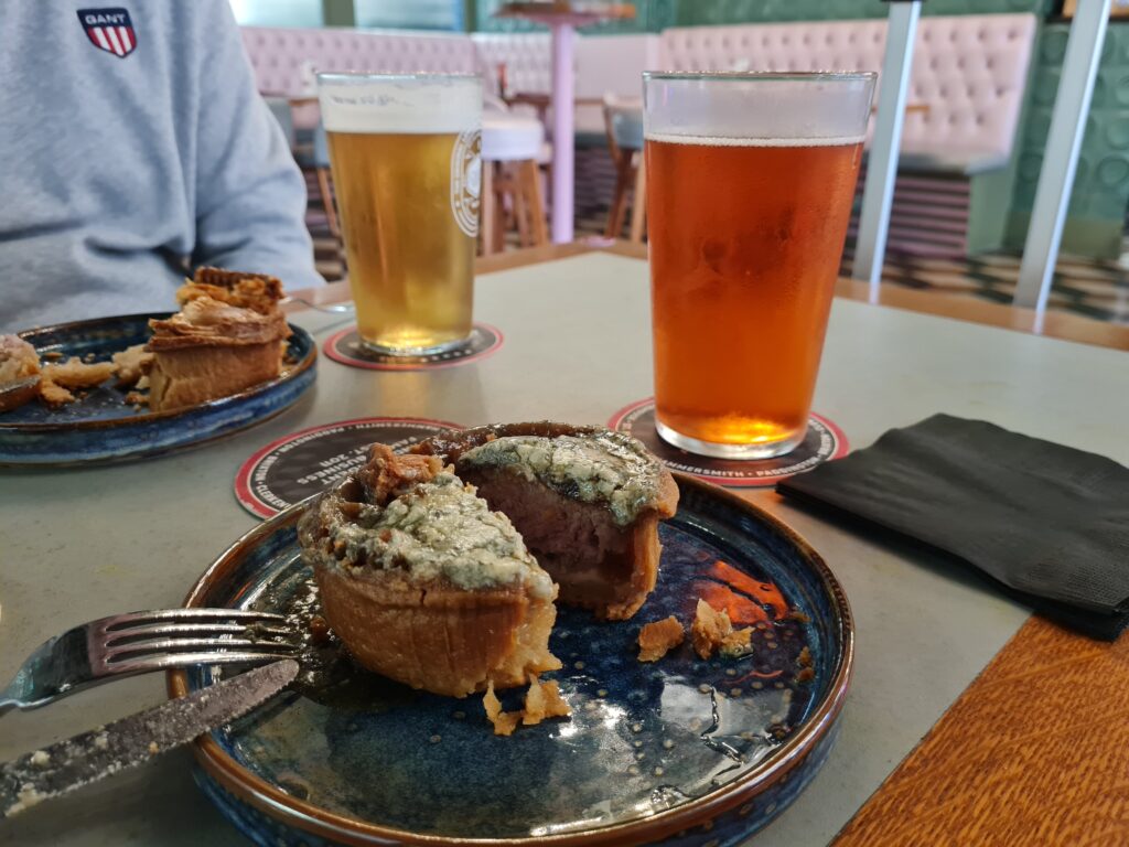 A pork pie with a blue cheese crust cut open on a plate, with two beers, at the Craft Beer Co., Hammersmith