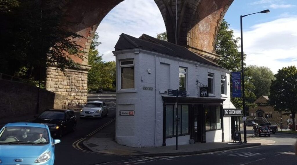 The Station House, a small white-painted corner pub on North Road in Durham, standing beneath an arch of the red brick railway viaduct