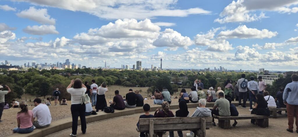The view over London from the top of Primrose Hill with people sitting on the crest