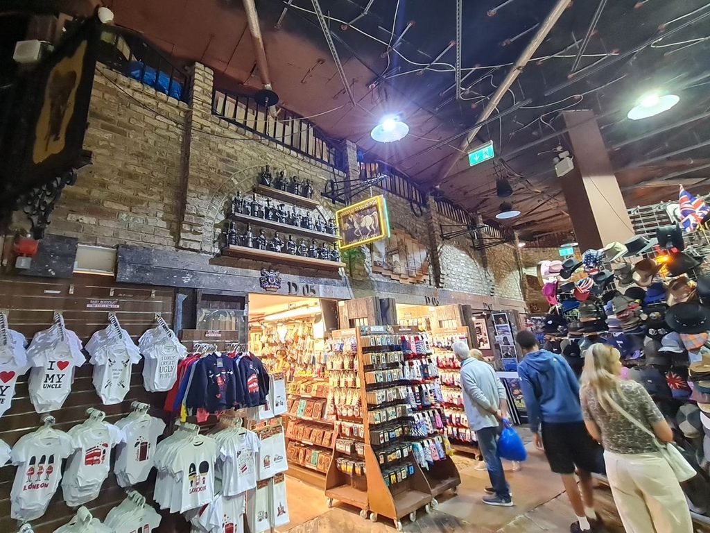 Stalls selling T-shirts and souvenirs under the brick and iron roof of Camden Market, London
