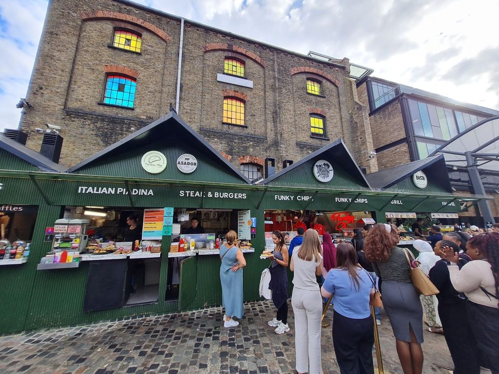 A queue at a green food stall in Camden Market selling Italian piadina, steaks and burgers, London