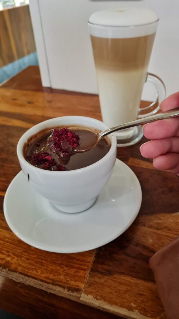 A latte in a tall glass and a cup of hot milk chocolate with dried cherry on a café table at Karmello, Kraków