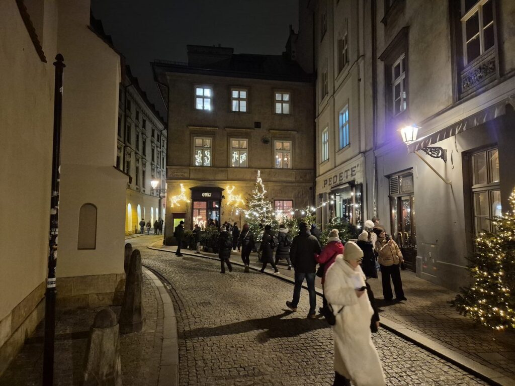 A cobbled side street in Kraków's Old Town at night with small Christmas trees outside the doors