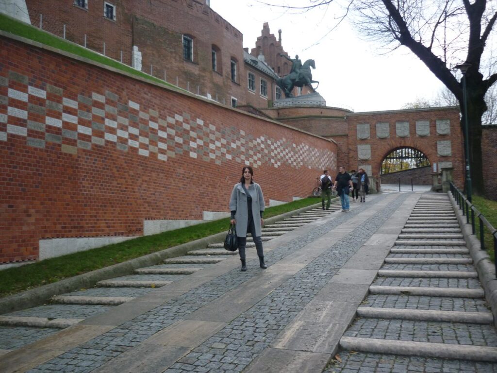 Olesia walking up the cobbled ramp to Wawel Castle beside the red brick walls, Kraków