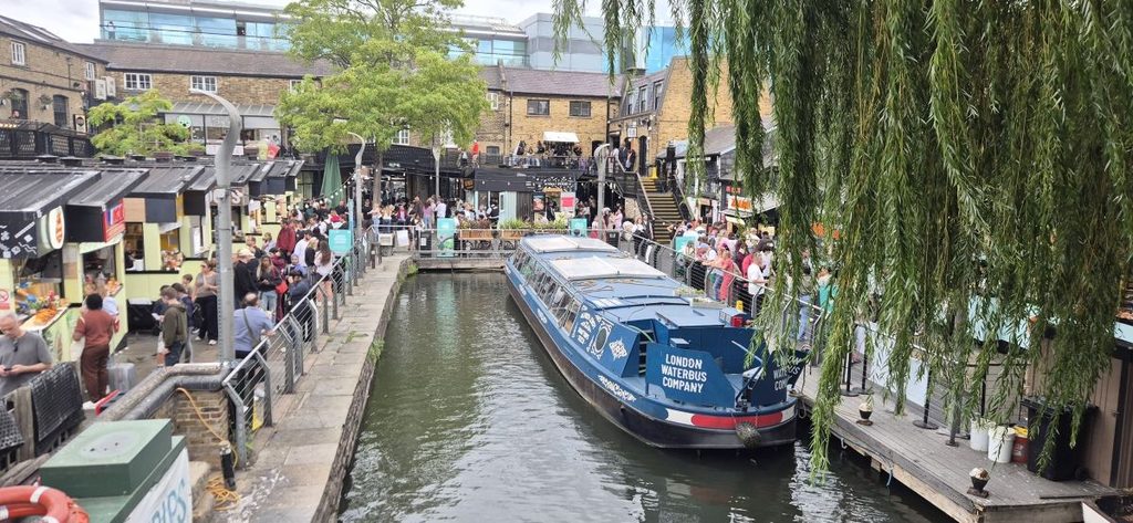 A narrowboat passing Camden Lock Market on the Regent’s Canal, with willows along the bank, London