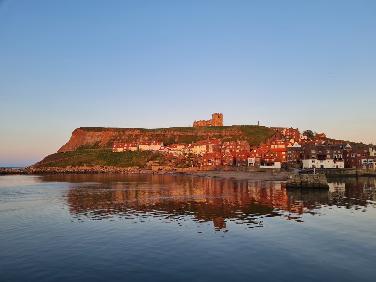 Whitby's East Cliff glowing at golden hour and reflected in flat water