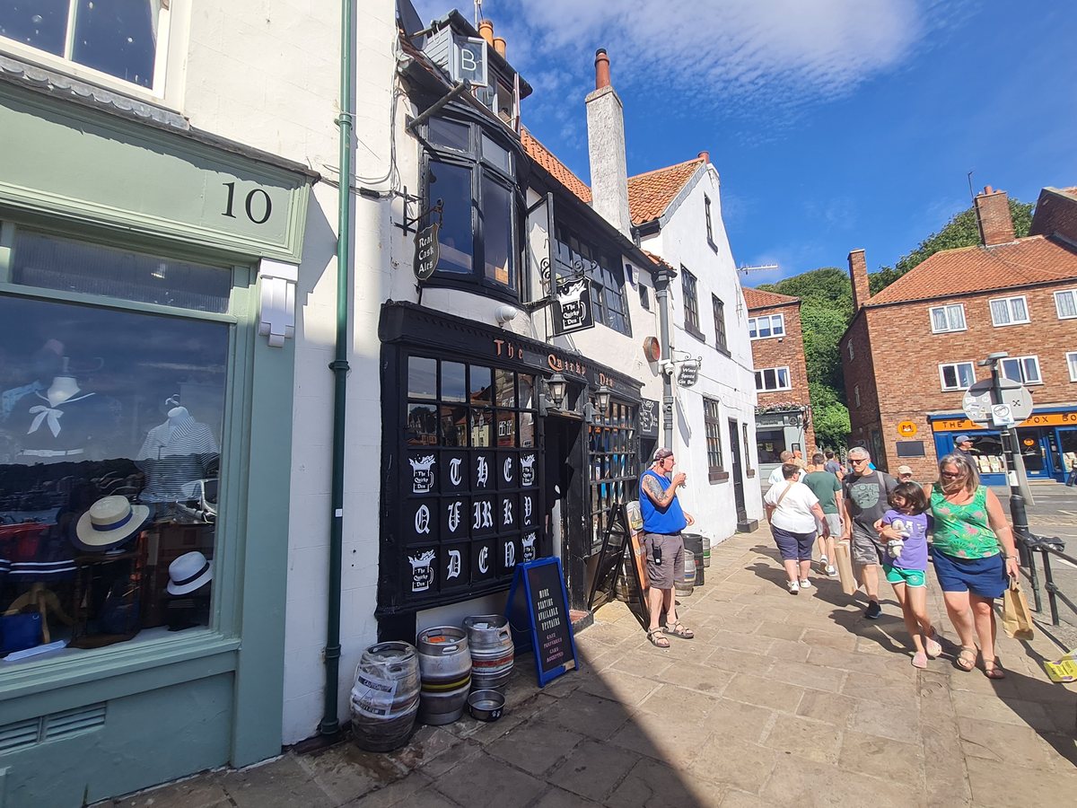 Black timber frontage of The Quirky Den micro pub with casks outside, Whitby